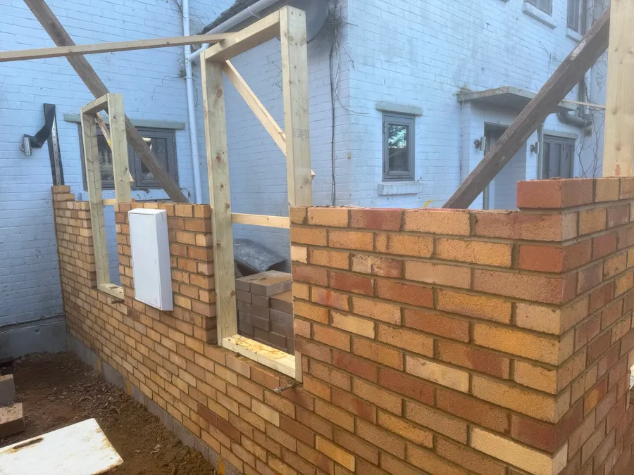 New brickwork for a house extension rising from the slab, with door and window openings framed ready for lintels